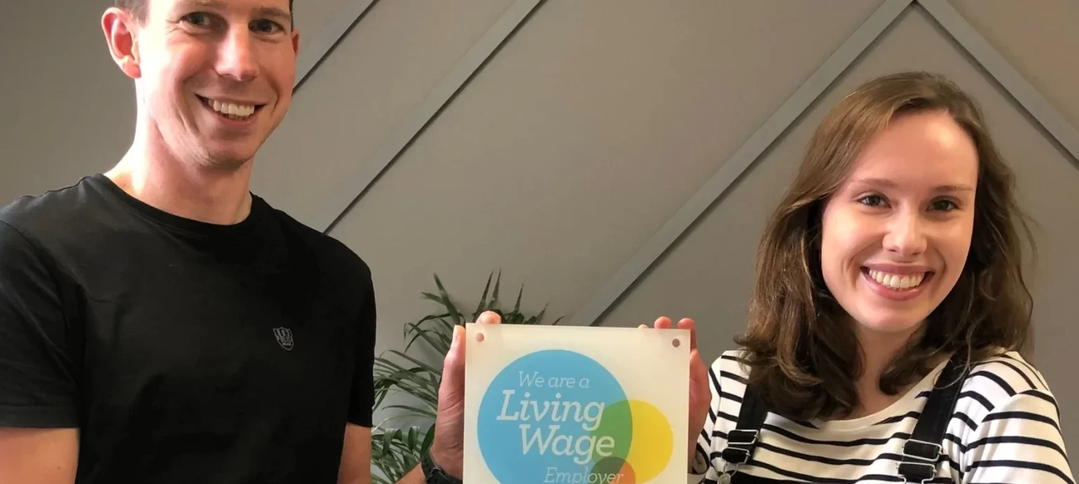 A man and a woman smiling holding a Living Wage Employer certificate