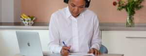 A lady wearing headphones in her kitchen, holding a pen and looking at a piece of paper