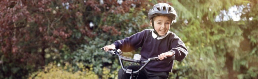 A boy wearing a helmet, smiling whilst riding a bicycle