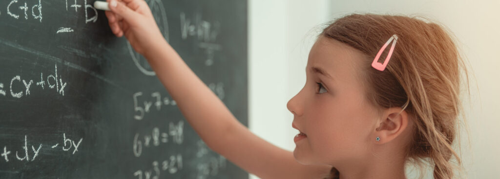 A girl writing maths equations using white chalk on a blackboard