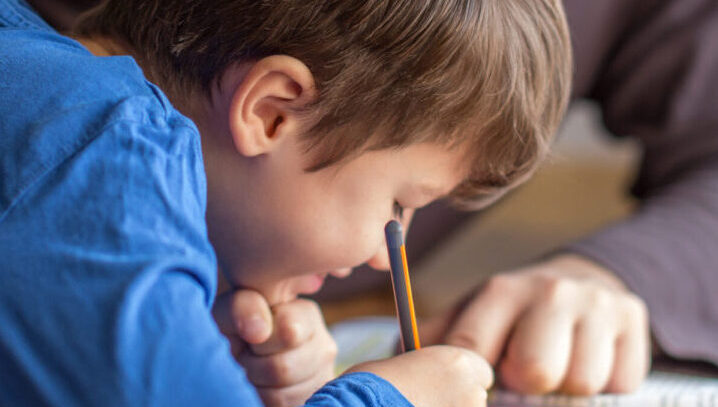 A child with brown hair smiling whilst writing in a text book