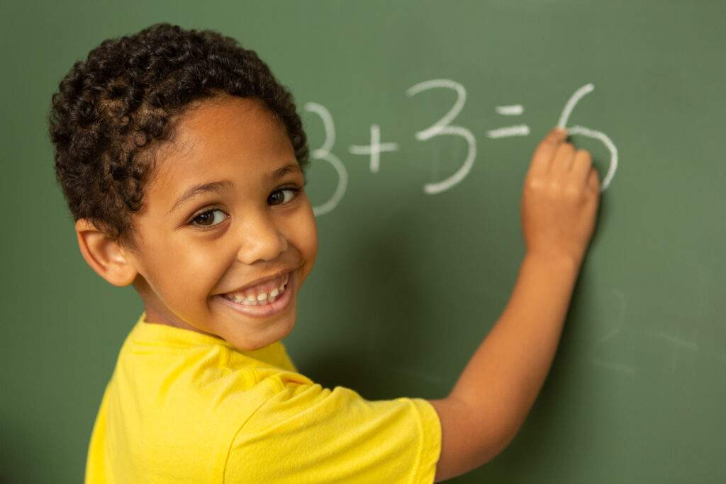 Elementary aged boy doing an addition problem on a chalkboard