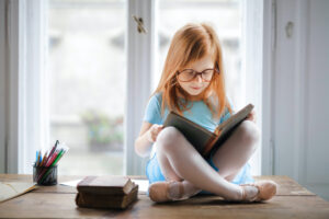 Girl reading a book whilst sat on a desk