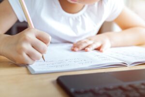 A kid is practicing and writing English cursive handwriting words in a notebook with online learning. Cursive handwriting practice. Pencil grasp activities. Kindergarten skills. Focus on pencil tip.