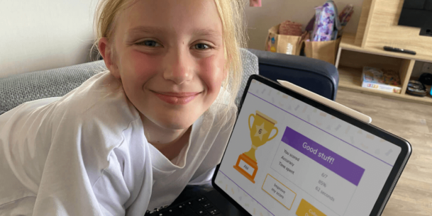 A blonde girl smiling in front of a laptop, showing a trophy and a good score on DoodleMaths